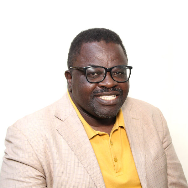 AMOS Action headshot A man wearing glasses, a light plaid blazer, and a yellow polo shirt sits against a plain white background, smiling at the camera.