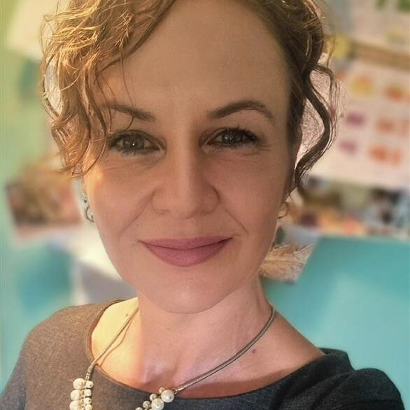 A woman with curly hair wearing a necklace, smiling at the camera.