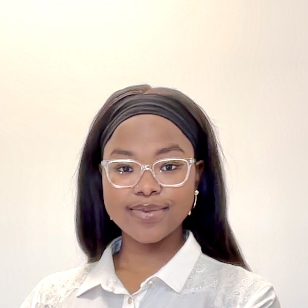 NGOBESE Mbali headshot A young Black woman with medium-brown skin and long, straight dark hair, worn loose with a wide black headband. She is wearing clear-framed glasses, gold drop earrings, and a cream blouse with lace detailing on the shoulders. Her expression is calm and confident, with a soft smile. The background is plain and light-coloured.