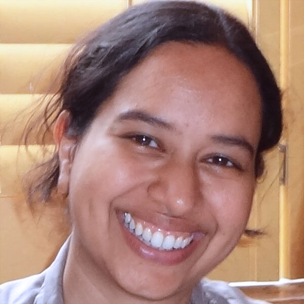This photo shows Savia de Souza, smiling, in front of a neutral background.